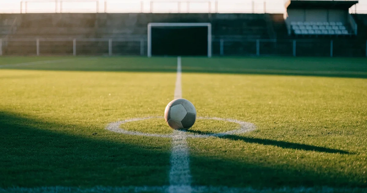 Ein Fussball liegt auf dem Mittelkreis eines Rasenfelds, die weissen Linien kreuzen sich auf dem gepflegten Gras im warmen Abendlicht.