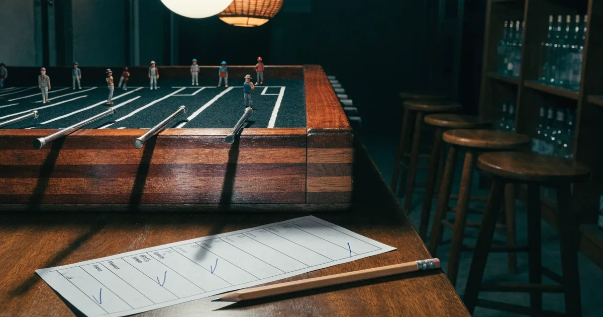 Ein hölzerner Tischfussball steht in einer leeren Bar, die Stangen mit den Figuren glänzen im Gegenlicht einer Lampe.