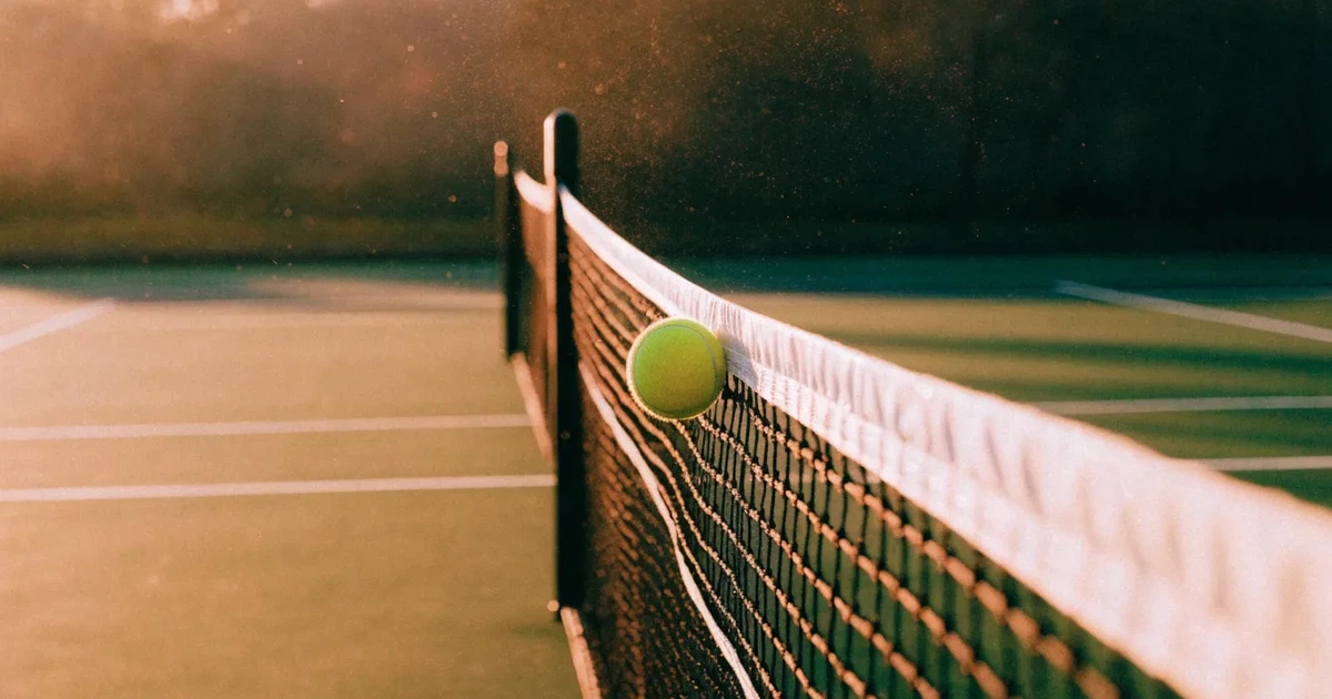 Ein Tennisnetz in Nahaufnahme im Gegenlicht der tiefstehenden Sonne, feine Staubkörner schweben über dem Platz.