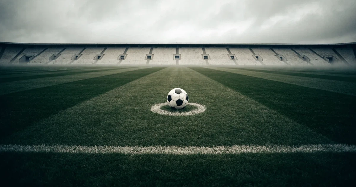 Ein Fussball liegt auf dem Anstosspunkt eines frisch gemähten Rasens, dahinter eine grosse Tribüne unter bewölktem Himmel