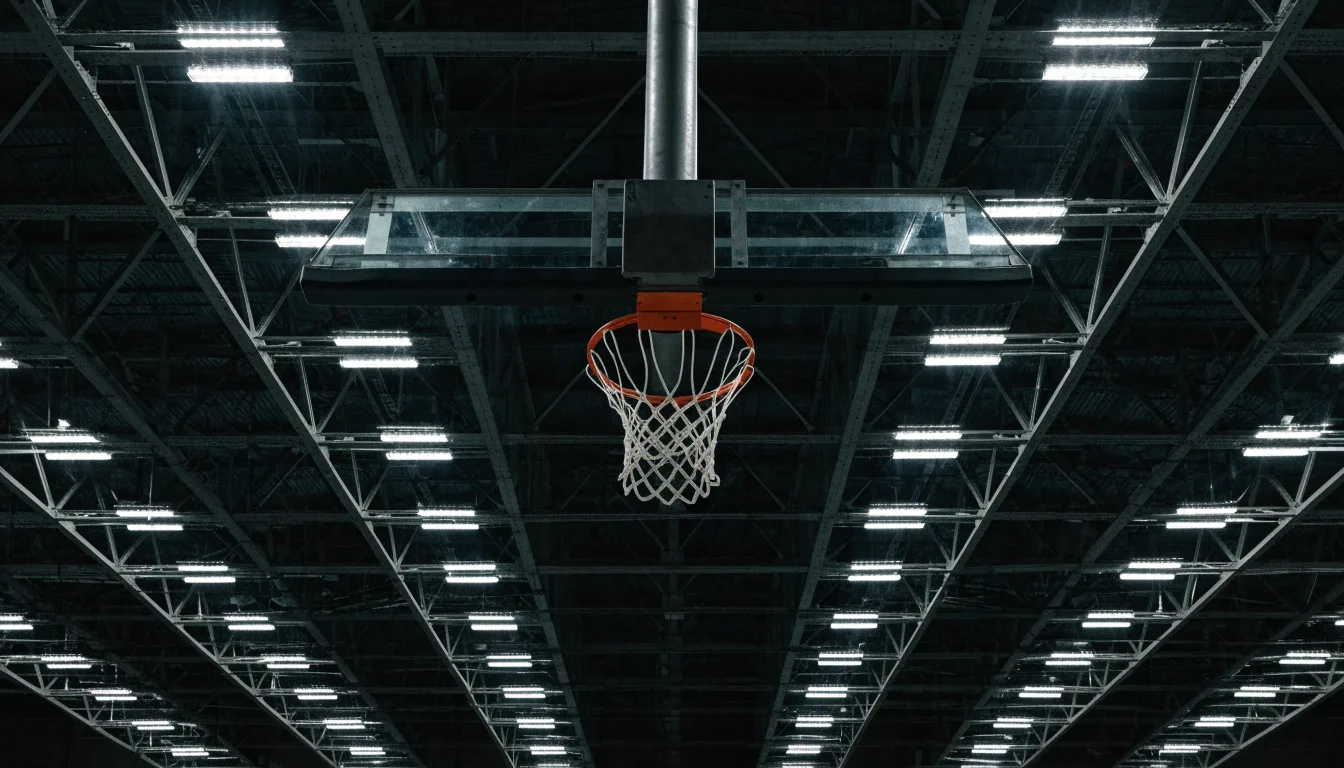 Ein Basketballkorb von unten gesehen, darüber eine Hallendecke mit Scheinwerfern und Stahlträgern.