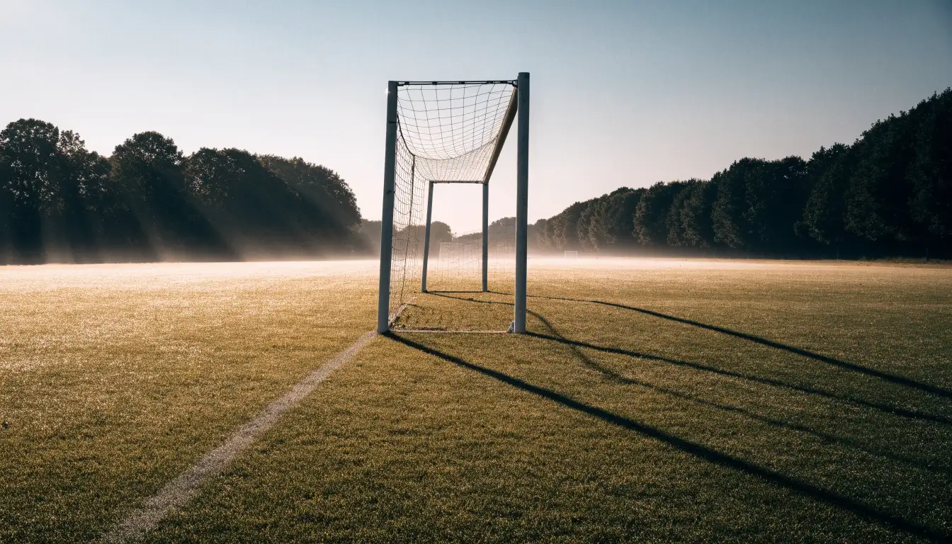 Ein Fussballtor mit Netz in der Totalen auf einem leeren Platz, Tau glänzt im Gras und die Morgensonne steht tief.