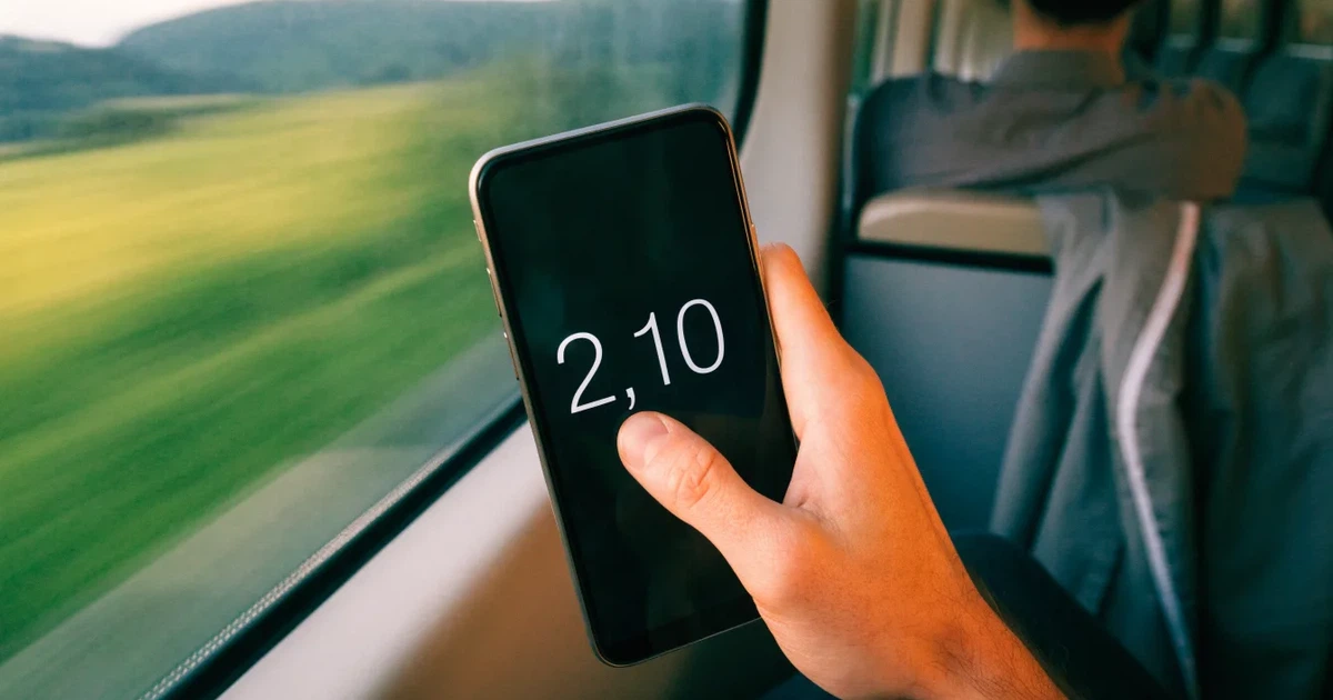 Eine Hand hält ein Smartphone mit schwarzem Bildschirm vor einem Zugfenster, draussen ziehen Hügel und Wiesen vorbei.