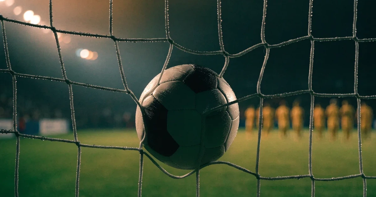 Ein Fussballnetz in Nahaufnahme, in dem ein Ball hängt, Wassertropfen glänzen auf den Maschen.