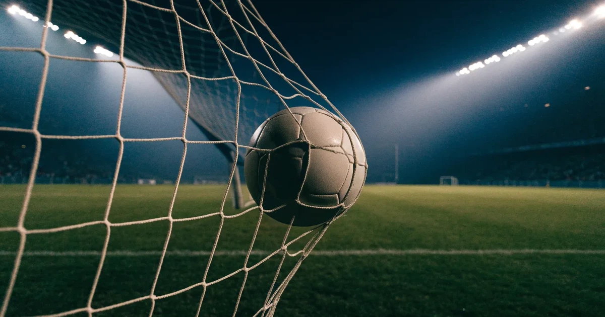 Ein Fussball liegt im Netz eines Tores, Flutlicht und kalte Abendluft liegen über dem leeren Platz